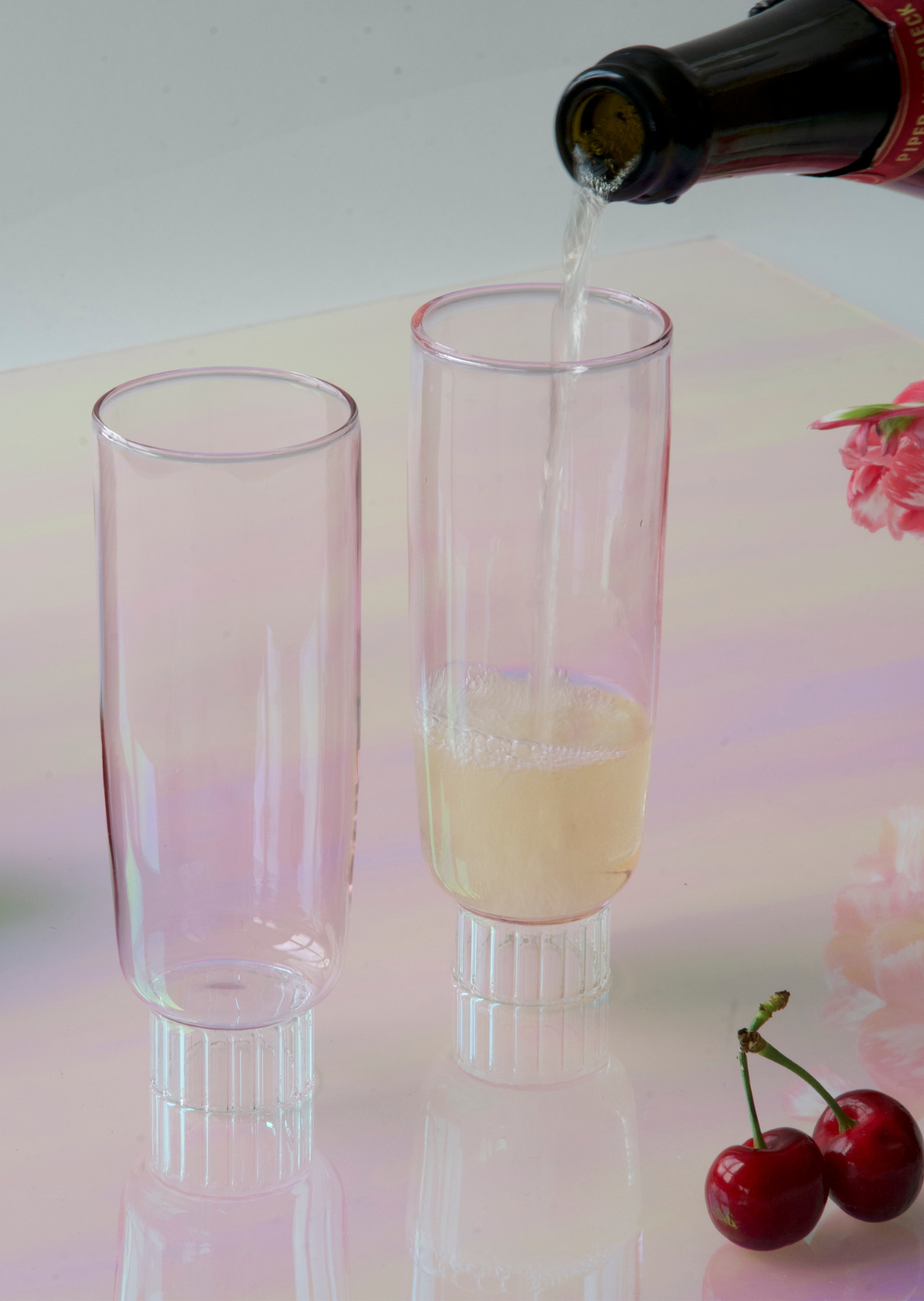 hand-blown colored champagne flutes in blush pinkon a table with cherries and champagne. A beautiful set ofof artist-designed champagne glassware