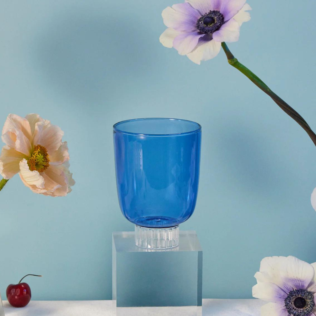 Set-of-four cobalt blue colored stemless wine glasses. A colored glass on a table with poppies and anemones flowers, cherries, raspberry tarts, rose strawberries, and grapes.