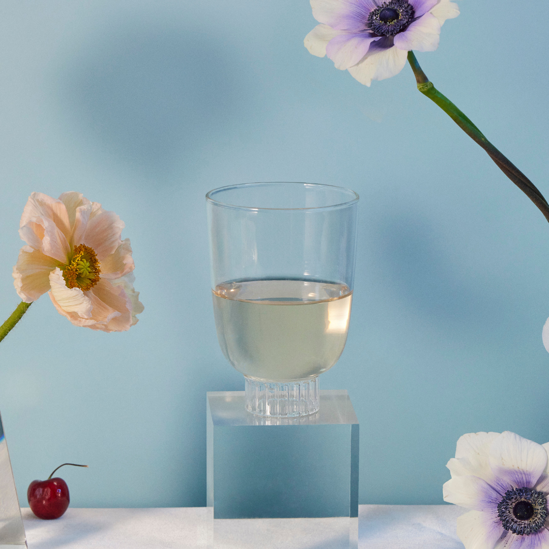 Sprezz romantic clear stemless wine glass on a table with poppies and anemones flowers, cherries, raspberry tarts, rose strawberries, and grapes. Made of 100% borosilicate which makes them lightweight yet durable and dishwasher safe