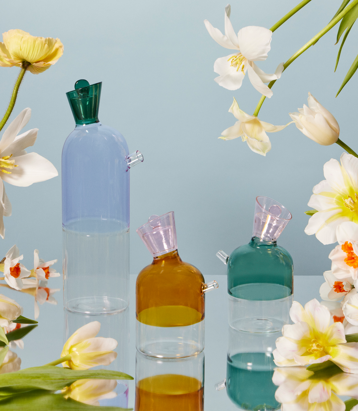 artist-designed, hand-blown colored glass water karafe and oil bottle on a table with flowers. A beautiful table setting