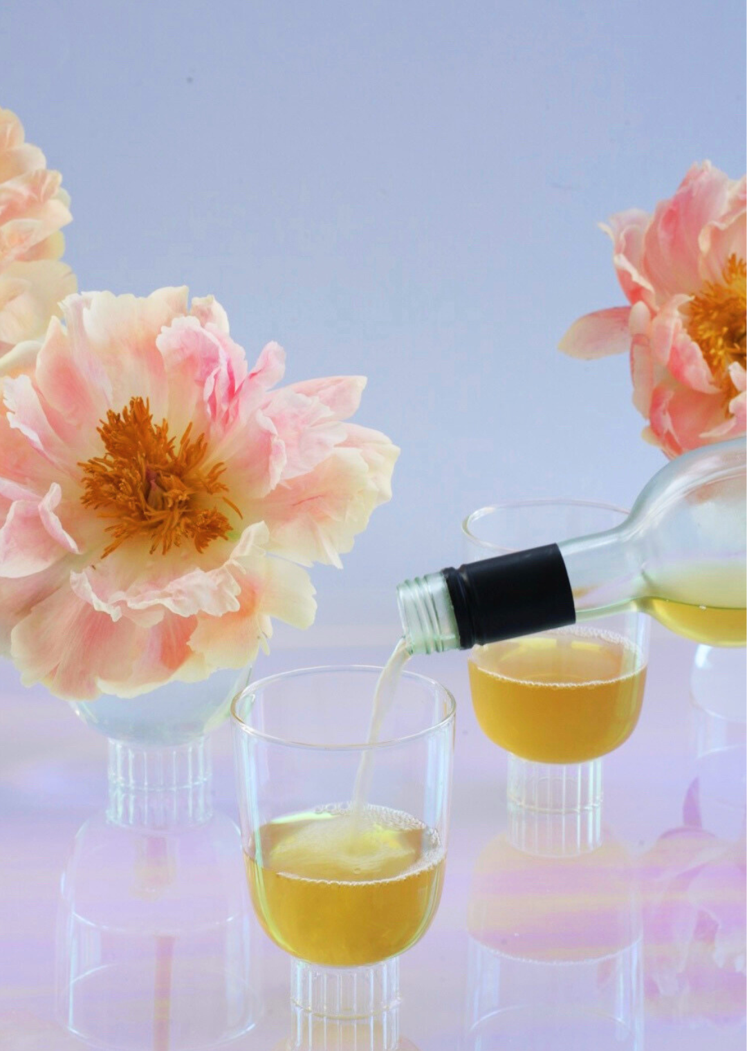 Two stemless wine glasses made from borosilicate glass on a table. Orange wine is being poured into one of Sprezz's stemless wine glasses, the other tinted glassware is already filled with orange wine. Treasured pieces that will become modern heirlooms.