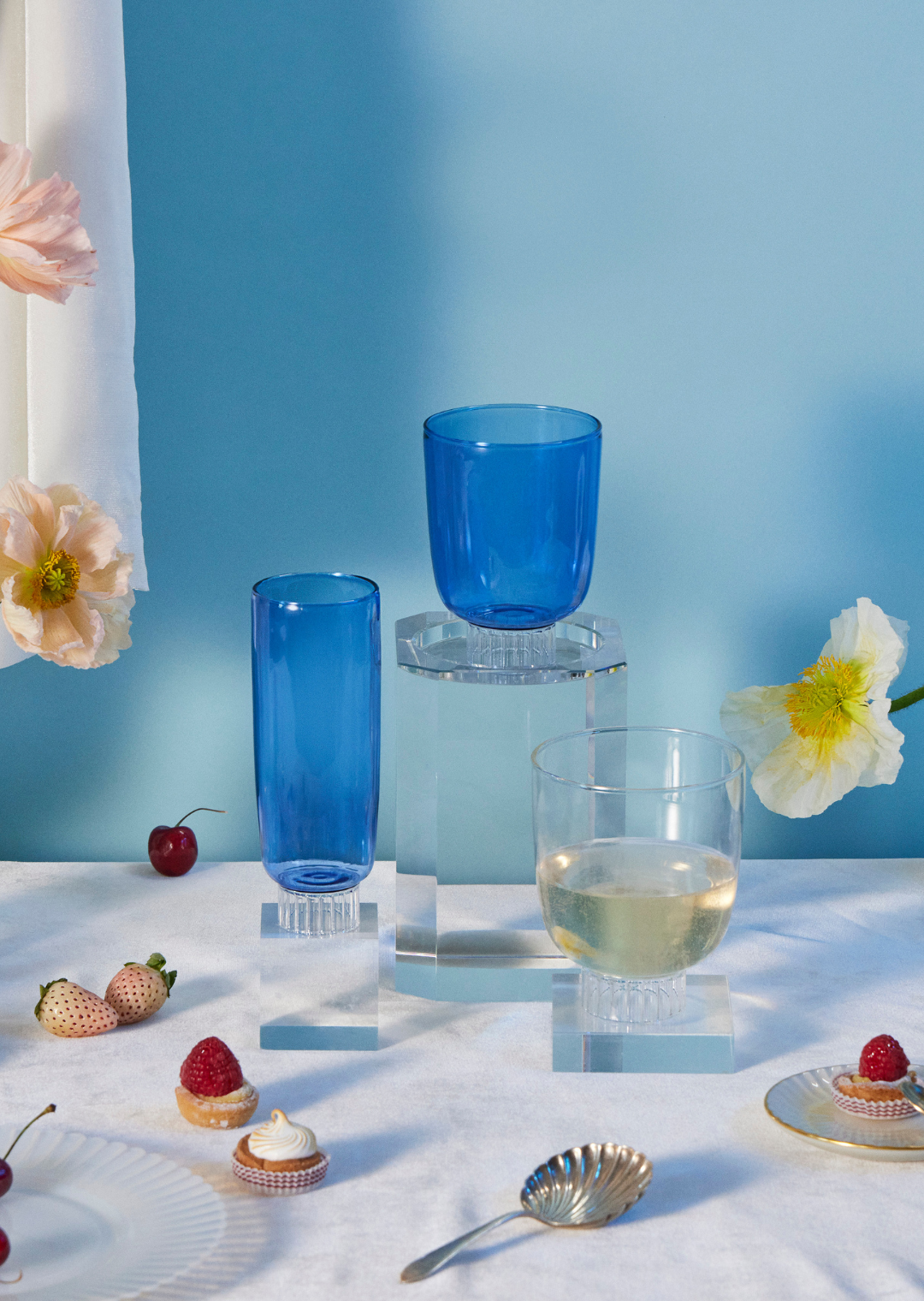 hand-blown colored champagne flutes and stemless wine glasses in cobalt blue on a table with flowers. A beautiful table setting of artist-designed glassware