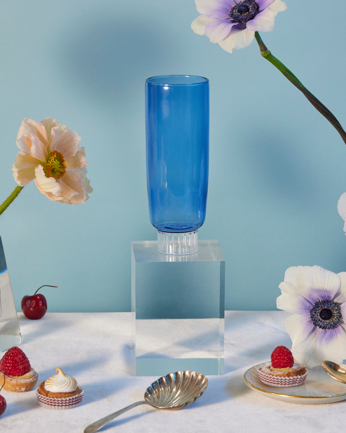 High-quality glassware and elegant tableware arranged on a dinner table, creating an ambiance of refined taste and romance. At the center of the composition stands a colored champagne flute, a tall blue glass that draws the eye with its vibrant hue and slender elegance.