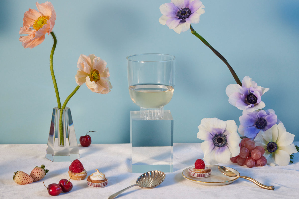 Premium borosilicate cocktail glass by Sprezz, on an elegant dinner table. This non-toxic and dishwasher-safe glassware is paired with a stunning arrangement of pink poppies and anemones. This rocks glass is a perfect blend of form and function for the seasoned host's memorable dinner party.