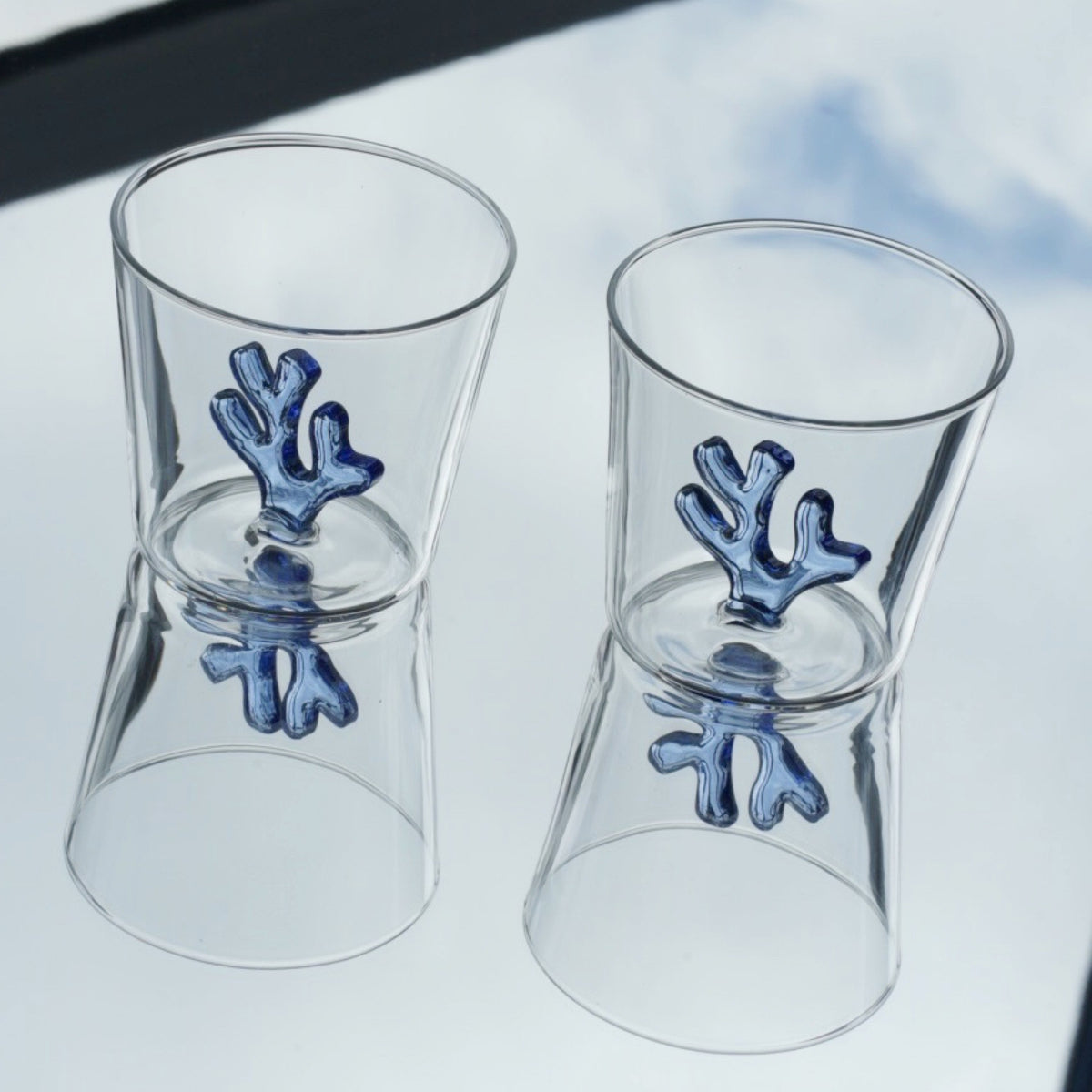 Two Sprezz colored glass drinkware with two blue corals on the inside. A collection of all-purpose clear coloured glassware in cobalt blue