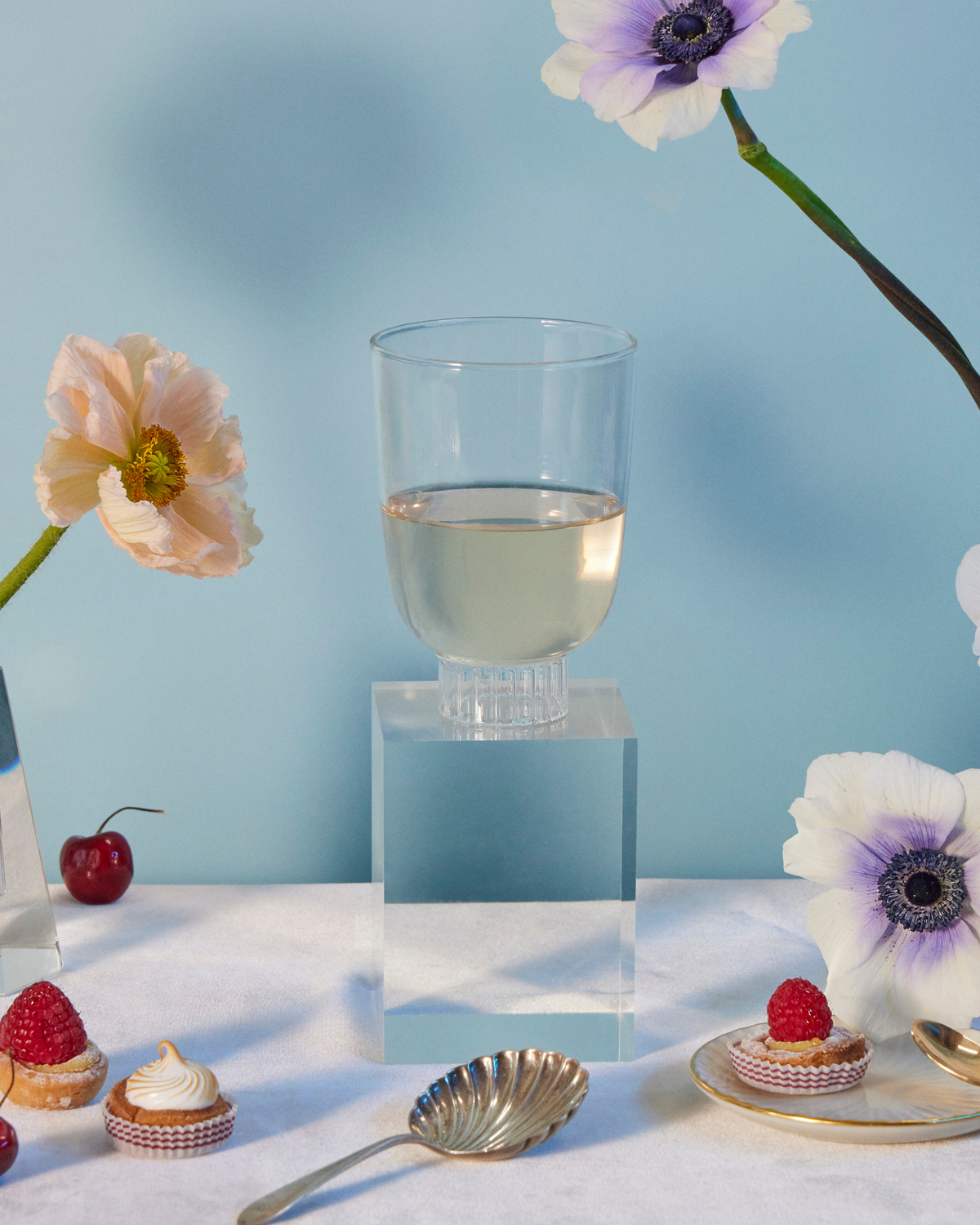 Sprezz romantic clear stemless wine glass on a table with poppies and anemones flowers, cherries, raspberry tarts, rose strawberries, and grapes. Made of 100% borosilicate which makes them lightweight yet durable and dishwasher safe 