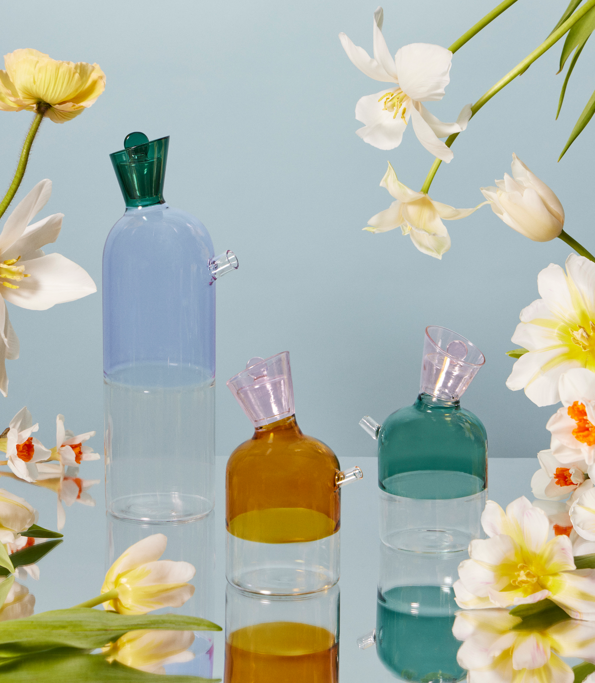  artist-designed, hand-blown colored glass water karafe and oil bottle on a table with flowers. A beautiful table setting